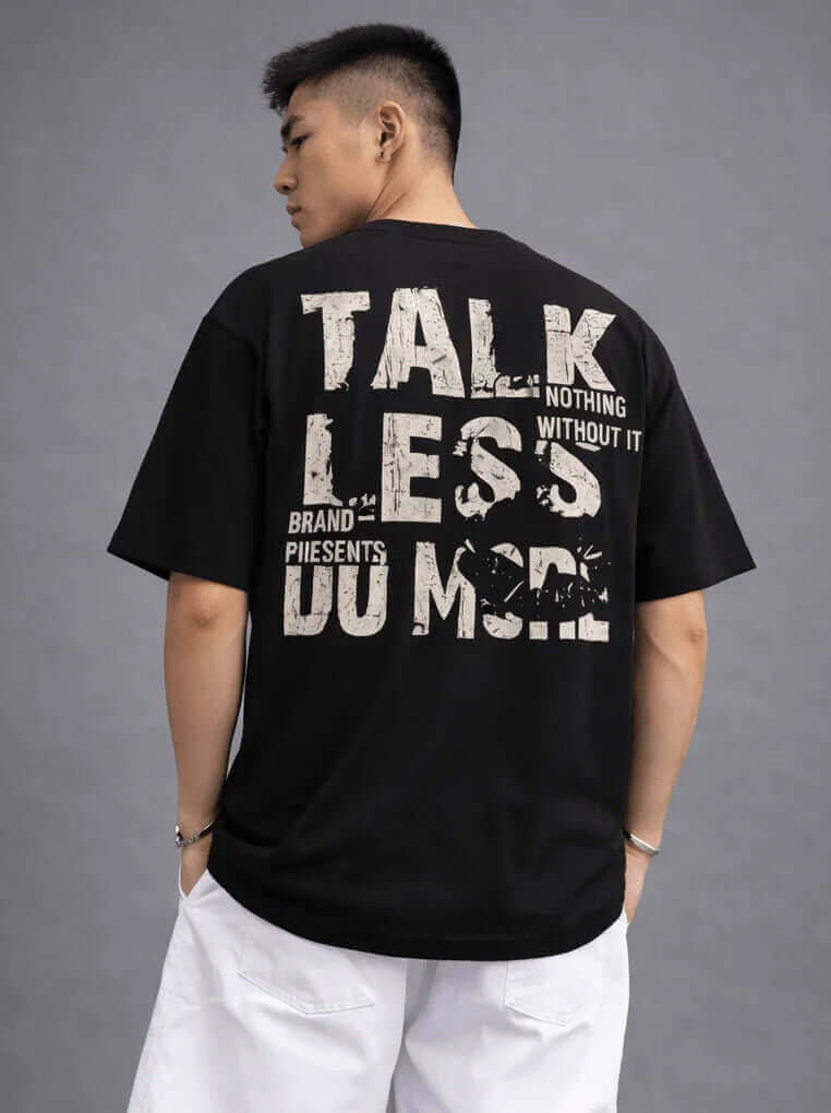 Man wearing oversized black streetwear T-shirt with bold 'TALK LESS DO MORE' graphic on back